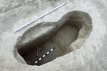 Archaeological excavations. Human remains (bone) in the excavated catacomb under ground, tomb with ritual burial. Measuring plank. Real digger process. Outdoors, copy space, close up.