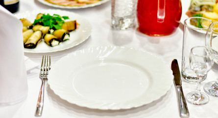 details of serving tables for a banquet in a restaurant. grapes, kiwi, tangerines, deli meats, white plates and white napkins. wine glass and vodka glasses on the table. selective focus