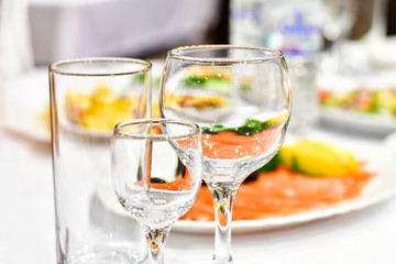 details of serving tables for a banquet in a restaurant. grapes, kiwi, tangerines, deli meats, white plates and white napkins. wine glass and vodka glasses on the table. selective focus