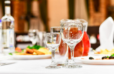 details of serving tables for a banquet in a restaurant. grapes, kiwi, tangerines, deli meats, white plates and white napkins. wine glass and vodka glasses on the table. selective focus
