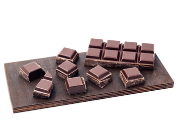 Chopped chocolate cubes, pieces of dark chocolate bar on a brown plank, isolated on white background