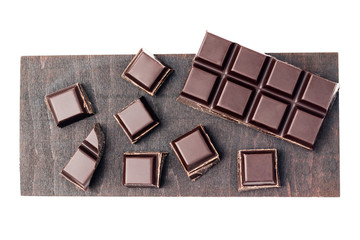 Chopped chocolate cubes, pieces of dark chocolate bar on a brown plank, isolated on white background, top view