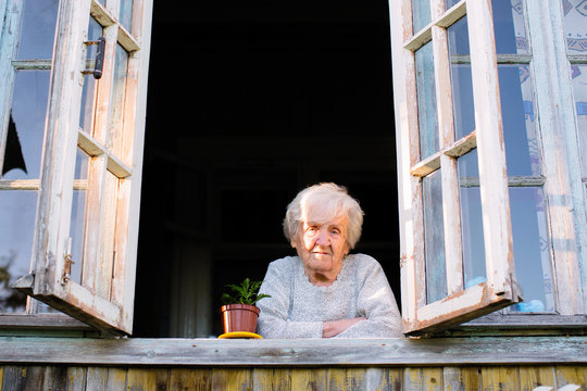 Elderly woman looks from window of a village house.