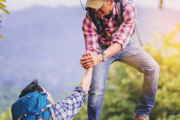 Young man with backpack helping friend to climb up to the top of mountain.