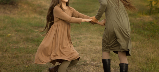 two girls running around, spinning on the grass in the park, in the woods. Climbing hands, a walk.