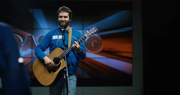 Medium shot of young man singing and playing guitar at casting