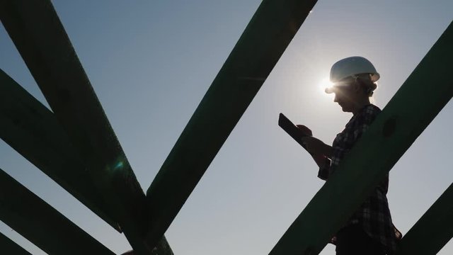 A young female engineer works with a tablet on the unfinished roof of a cottage