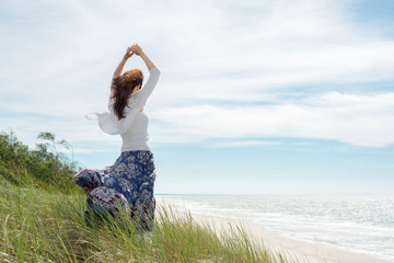 Young brunette woman in dress stands on the hill by the sea