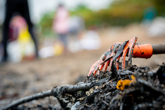 Closeup orange rake on pile of dirty waste on blurred background of volunteer clean up beach. Beach environmental pollution concept Tidying up rubbish on beach. Ocean garbage. Coast polluted.
