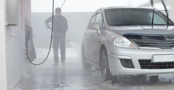 A man washes a shower of a soaped car at a car wash in the winter. A cold season.