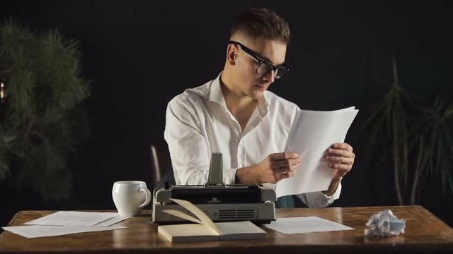 Young writer has already typed up last pages of new, exciting book, real professional rereading the text to make sure that everything done perfectly, indoor shoot in modern apartment with black walls