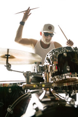 Professional drummer behind the drum kit on a white background in shirt, glasses and cap