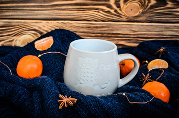 Big white cup of cocoa on the blue knitted sweater with vibrant orange tangerines and anise seeds around at the brown wooden background.Concept of autumn winter season. Warm drink at cozy atmosphere