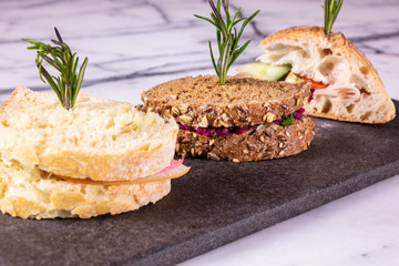 Three sandwiches with salad, ham, cheese and tomatoes on marble table.