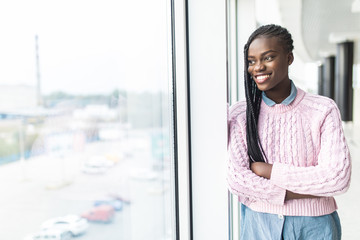 Attractive young african businesswoman staring thoughtfully through office windows at the city skyline