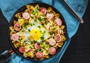 fried eggs with pasta farfalle, sausage and cheese in a frying pan