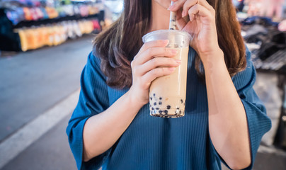Fototapeta premium A young woman is drinking a plastic cup of bubble milk tea with a straw at a night market in Taiwan, Taiwan delicacy, close up.
