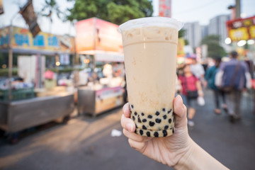 A young woman is holding a plastic cup of brown sugar bubble milk tea at a night market in Taiwan, Taiwan delicacy, close up.