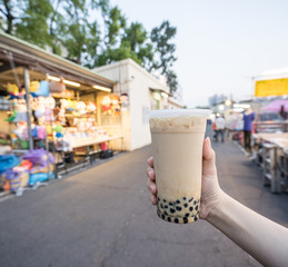 A young woman is holding a plastic cup of brown sugar bubble milk tea at a night market in Taiwan,...
