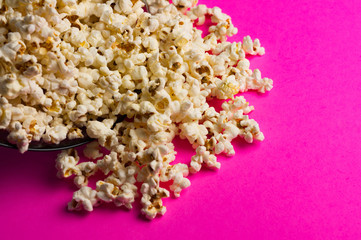 Fried popcorn scattered from glass plate on pink background with copy space. Сoncept of leisure