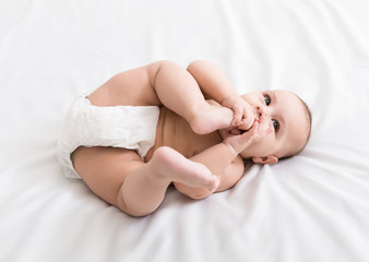 Adorable little baby sucking foot lying on bed