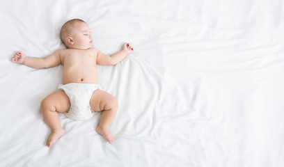 Newborn baby napping on white blanket with his arms up.