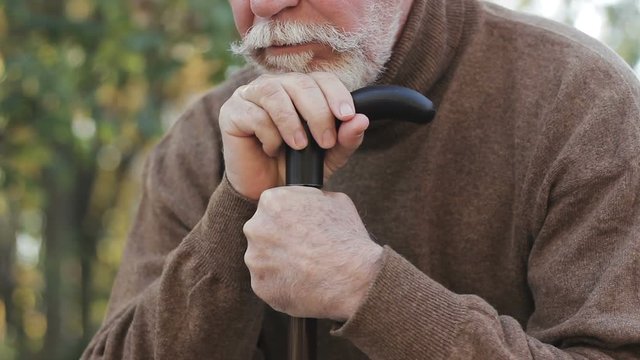 Thoughtful, tired grey-haired grandfather, bending on cane, moving difficulty