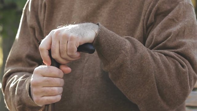 Aged man having nervous system disease, hands shaking strongly, leaning on cane