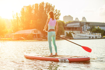 Woman is floating on a SUP board on sunny morning. Stand up paddle boarding - awesome active recreation during vacation.