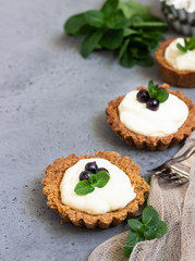 Mini tarts (tartlets) with whipped cream or custard and fresh berries served with mint. Homemade dessert. Grey background. Copy space.