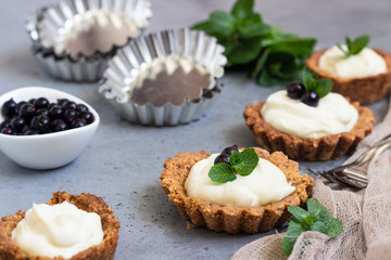 Obraz na płótnie Canvas Mini tarts (tartlets) with whipped cream or custard and fresh berries served with mint. Homemade dessert. Grey background. Copy space.