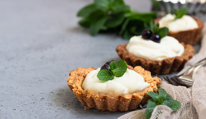 Mini tarts (tartlets) with whipped cream or custard and fresh berries served with mint. Homemade dessert. Grey background. Copy space.