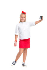 Full length portrait of cute little kid girl in stylish clothes looking at camera and smiling, standing against white studio wall with retro camera. Kids fashion concept