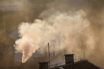 Smoking chimneys at roofs of houses emits smoke, smog at sunrise, pollutants enter atmosphere. Environmental disaster. Harmful emissions and exhaust gases into air. Fog, winter day, heating season. - obrazy, fototapety, plakaty