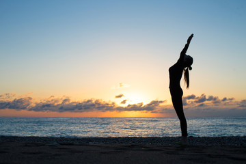 Female silhouette greeting to the rising sun on the beach in the morning