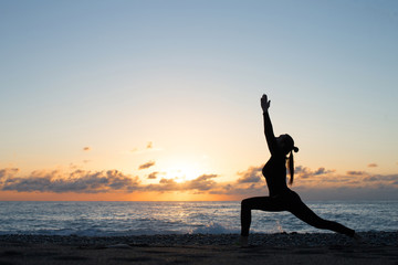 Fototapeta na wymiar Human silhouette doing yoga on the beach in front of rising sun