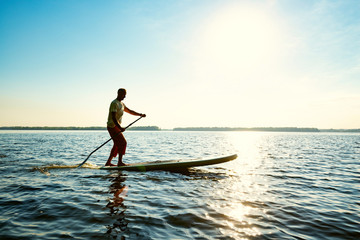 Fototapeta na wymiar Joyful guy paddling on a SUP board