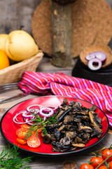 Fried mushrooms, onion and cherry tomatoes on a plate on a wooden table