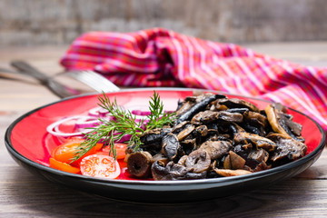 Fried mushrooms, onion and cherry tomatoes on a plate on a wooden table