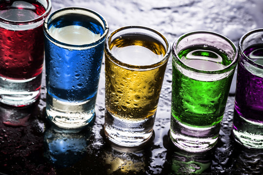 Colorful alcohol in transparent glass vodka shots on wet bar surface. Celebrating weekend patry background.