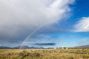 rainbow over field with blue sky and clouds