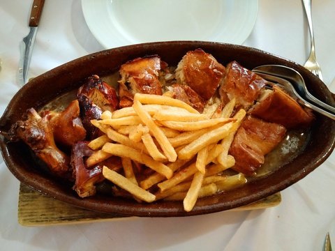 Roast suckling pig (Cochinillo Asado) served with fried potatoes and gravy at a typical Spanish restaurant, Segovia, Spain