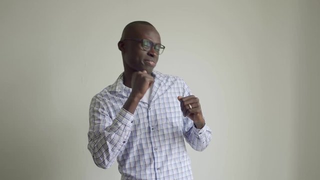 Happy african american man dancing and smiling at camera. Cheerful young man in checkered shirt and eyeglasses dancing and laughing on grey wall background. Celebration concept