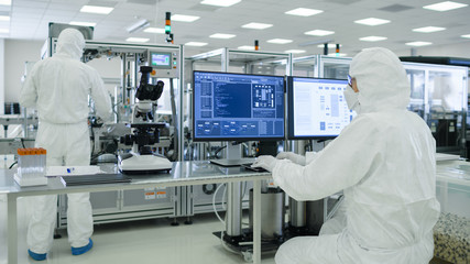Shot of a Scientists in Sterile Suits Working with Computers, Analyzing Data form Modern Industrial Machinery in the Laboratory. Product Manufacturing Process: Pharmaceutics, Semiconductors. - obrazy, fototapety, plakaty
