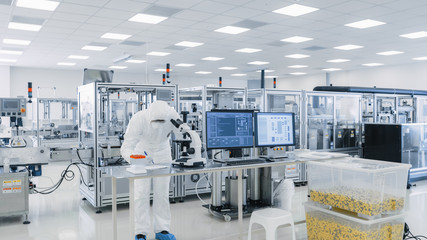 Shot of Sterile High Precision Manufacturing Laboratory where Scientists in Protective Coverall's Use Computers and Microscopes, doing Pharmaceutics, Biotechnology and Semiconductor Research.