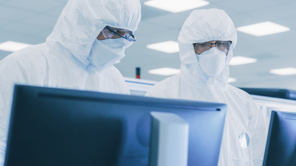 Two Scientists/ Technicians in Sterile Suits Check Data on Personal Computer, the Have Discussion. They Work in Pharmateutics Manufacturing Laboratory.
