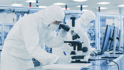 In Laboratory Scientist in Protective Clothes Doing Research, Using Microscope and Writing Down...