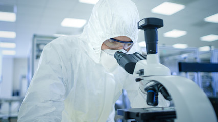 In Laboratory Scientist in Protective Clothes Doing Research Uses Microscope. Modern Manufactory Producing Semiconductors and Pharmaceutical Items.