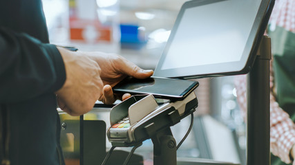 In the Supermarket Close-up Footage of the Man Paying with Smartphone at the Checkout Counter. Using Modern and Convenient Wireless NFC Paying System in Big Mall.