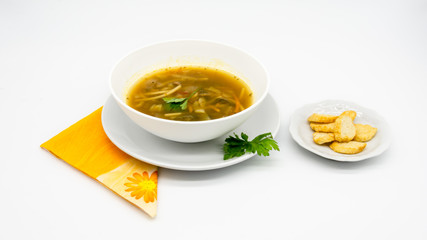 A delicious soup dish with pasta, toasted bread and vegetables, decorated with parsley, over a orange napkin and with a large and clean white background